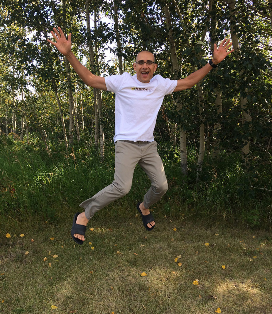 Smiling man jumps joyfully outdoors beside leafy trees