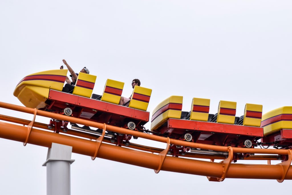 Riders on colorful roller coaster against cloudy sky