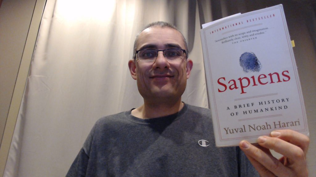 Man holding Yuval Noah Harari's Sapiens book