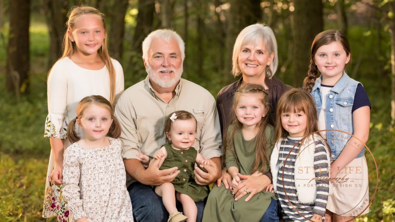 Grandparents pose outdoors with six smiling granddaughters