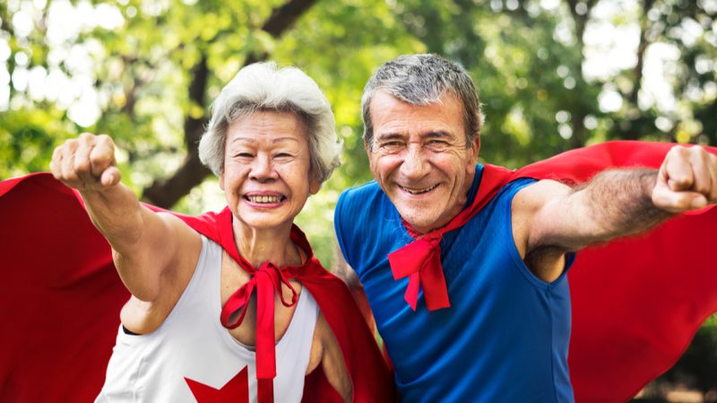 Smiling senior couple wearing red superhero capes outdoors
