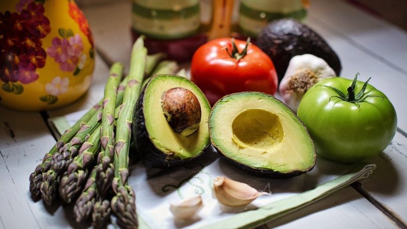 Avocado halves, asparagus, tomatoes, garlic, and olives on table