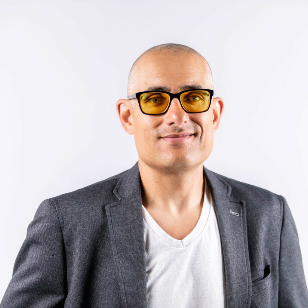 Smiling bald man wearing yellow-tinted glasses and gray blazer