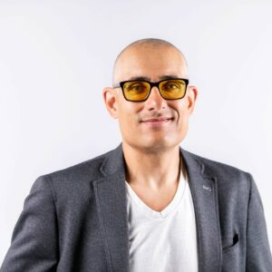 Smiling bald man wearing yellow-tinted glasses and gray blazer