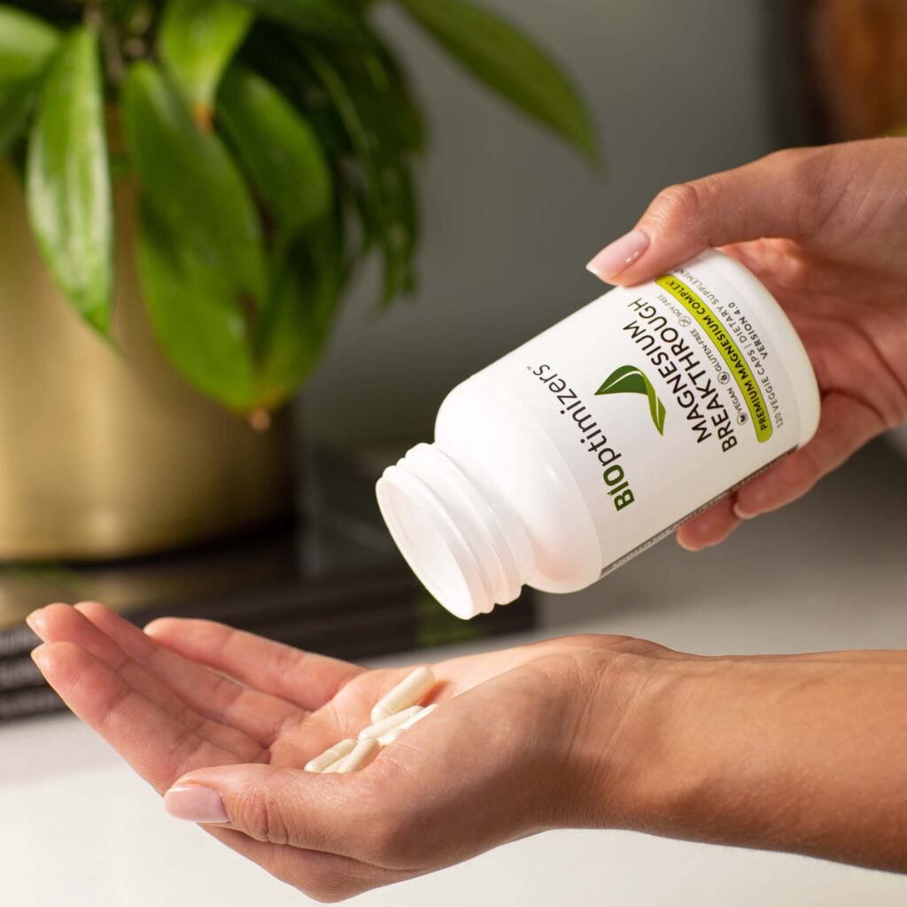 Hands pouring magnesium supplement capsules from a white bottle