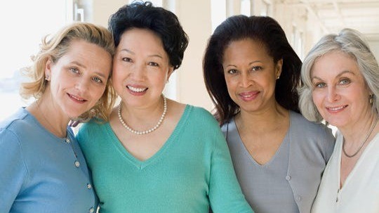 Four smiling middle-aged women standing closely together indoors
