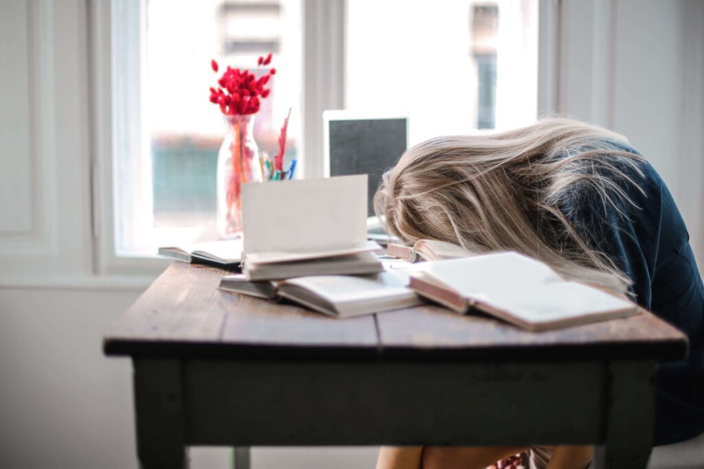 Student asleep at desk surrounded by open books